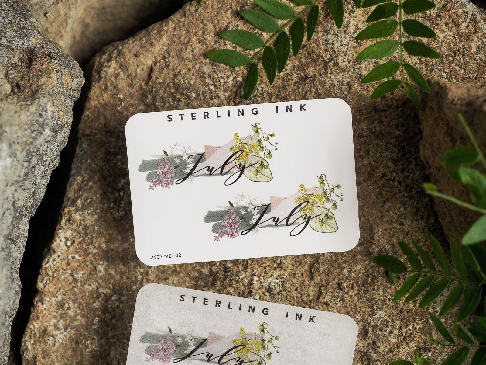 Watercolor floral sticker for July, featuring delicate pastel pink and green foliage surrounding the elegantly scripted month name.