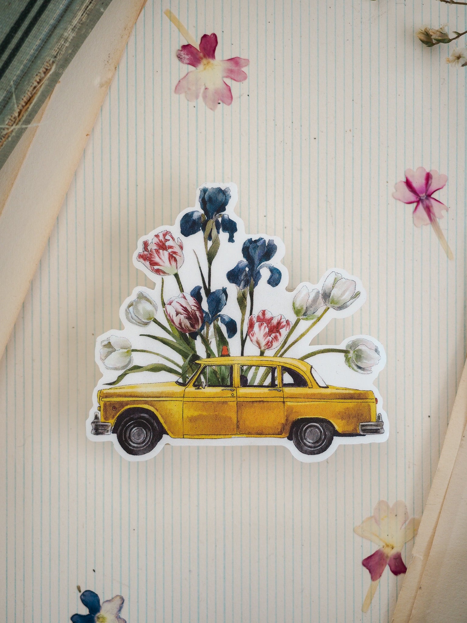 A charming sticker featuring a bright yellow retro sedan nestled among a vibrant bouquet of blue, pink, and red flowers.