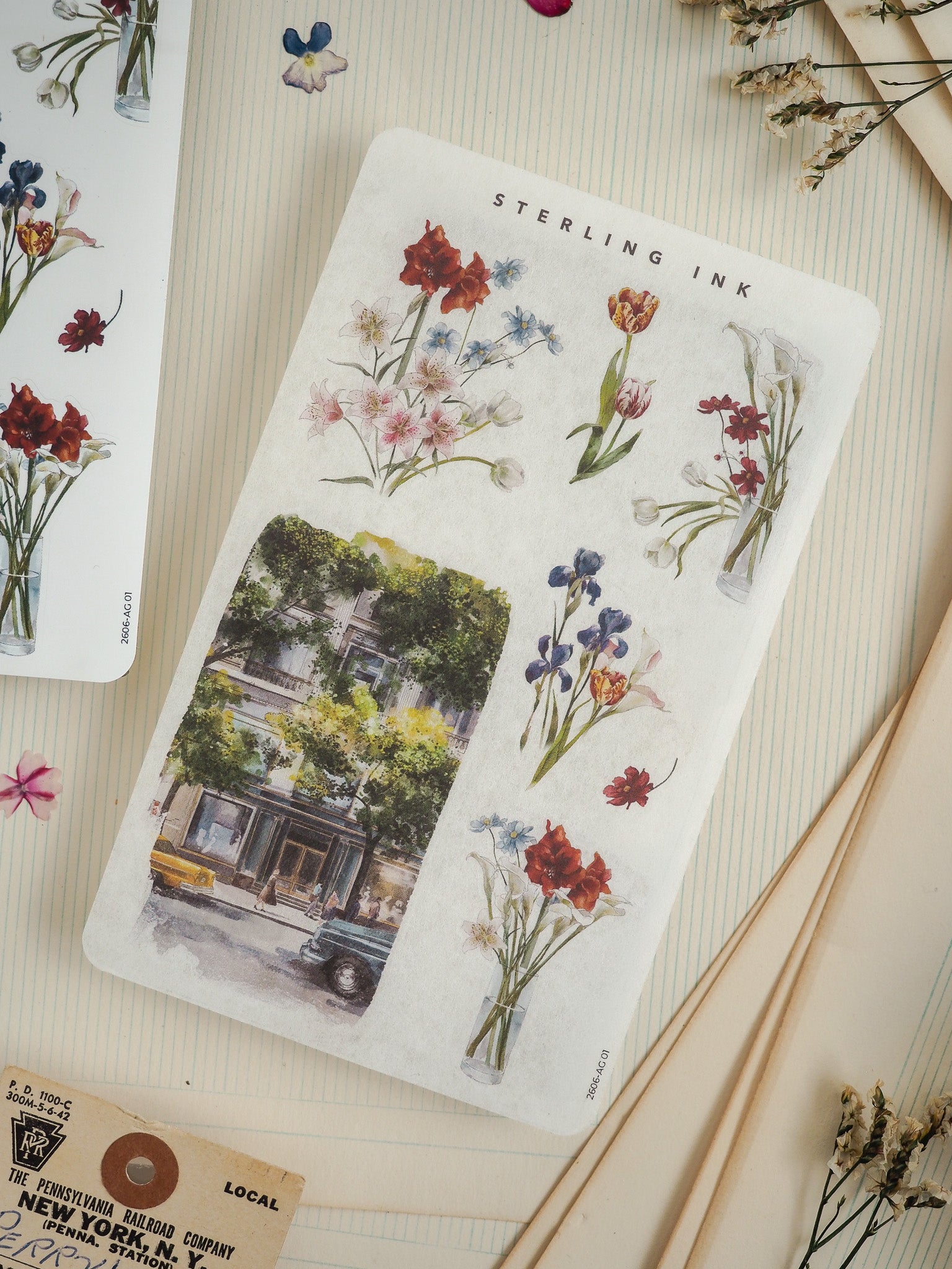 Watercolor illustration card titled "Sterling Ink," featuring a vintage street scene beneath a border of detailed, colorful botanical drawings of flowers.