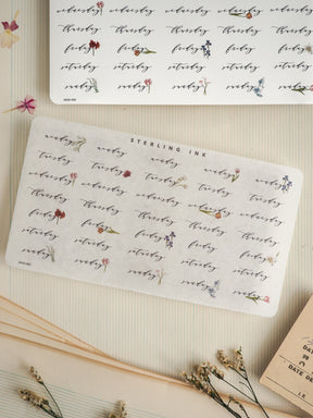 Decorative patterned sticker sheet featuring the days of the week and "Sterling Ink," printed in black ink with small complementary floral motifs for journaling.