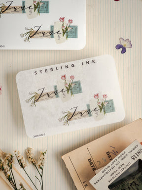 Cream-colored stationery printed with "STERLING INK," featuring elegant handwritten "july" script and delicate watercolor floral sprigs in pink and green tones.
