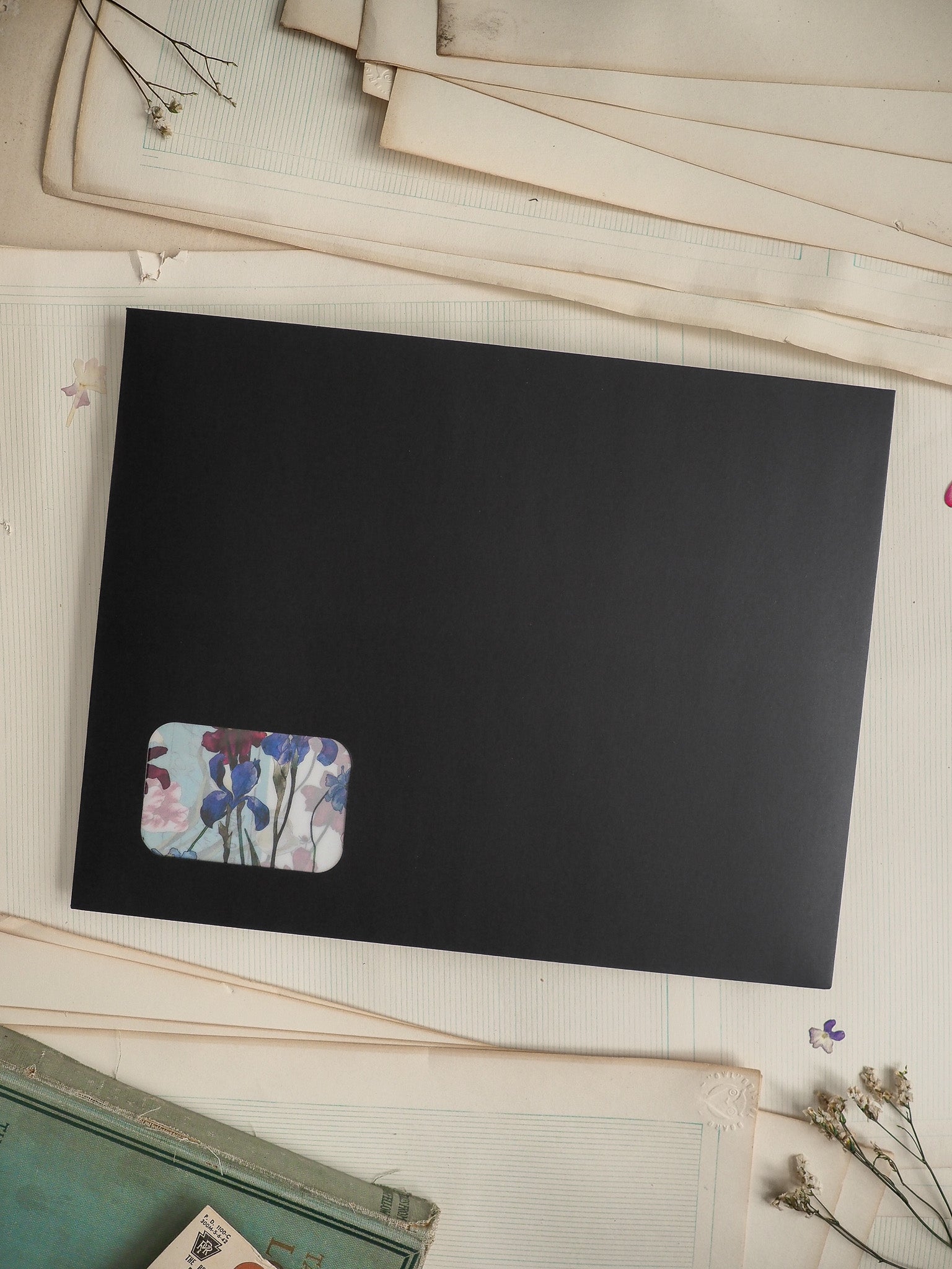 Black card displaying a cute, rectangular floral sticker featuring blue, purple, and white spring flowers and green stems.