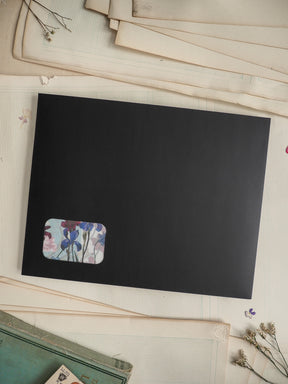 Black card displaying a cute, rectangular floral sticker featuring blue, purple, and white spring flowers and green stems.