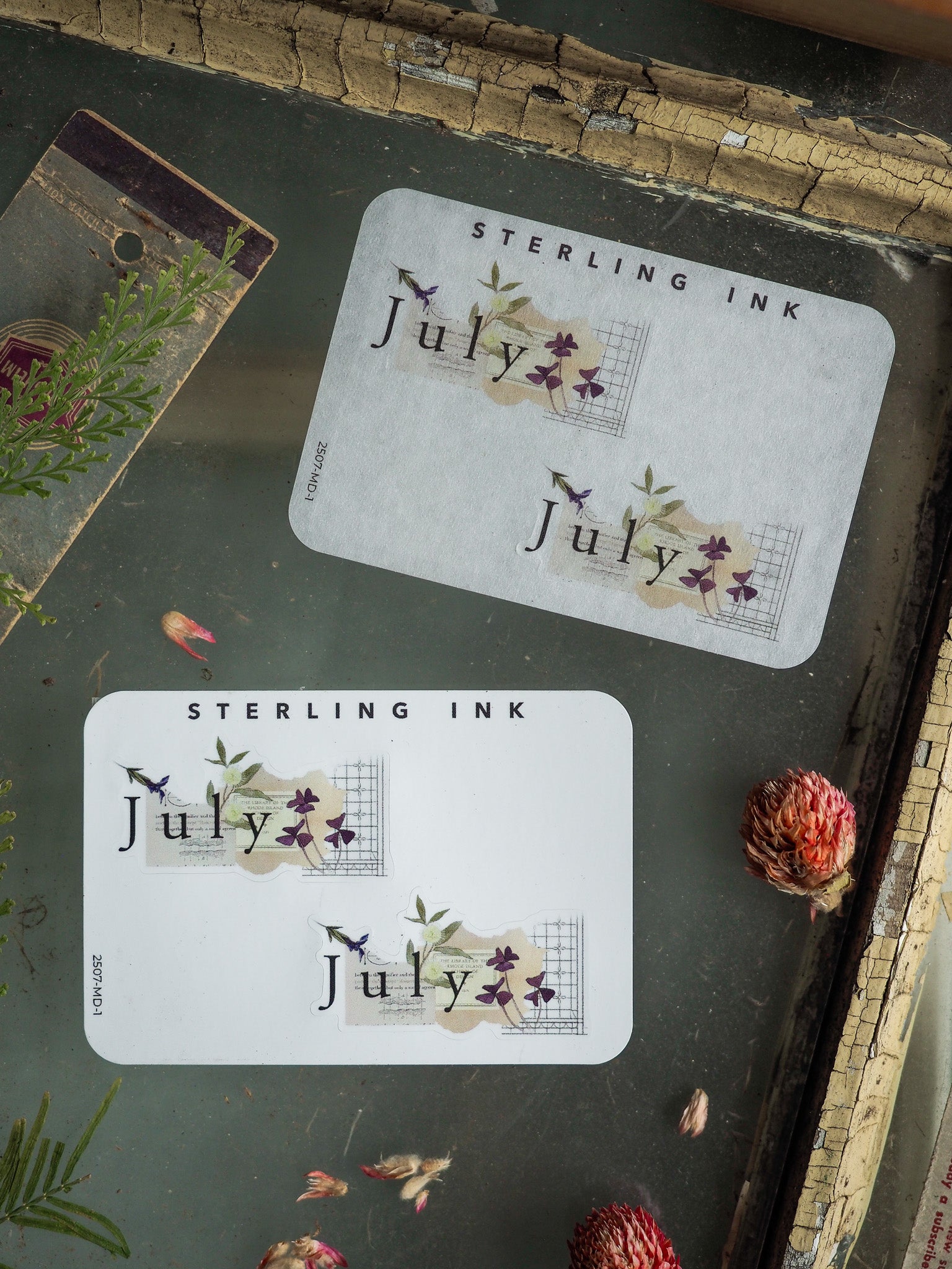 Elegant white sticker sheets featuring the month of July and delicate watercolor illustrations of purple flowers, green foliage, and the "Sterling Ink" brand name.