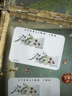 Elegant July 2025 month sticker featuring beautiful calligraphy, accented with purple and green watercolor foliage and a delicate grid frame for journaling.