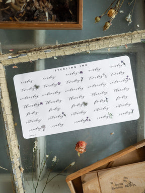 Decorative white planning stickers featuring black ink labels for all seven weekdays, ideal for organizing and tracking schedules for July 2025.