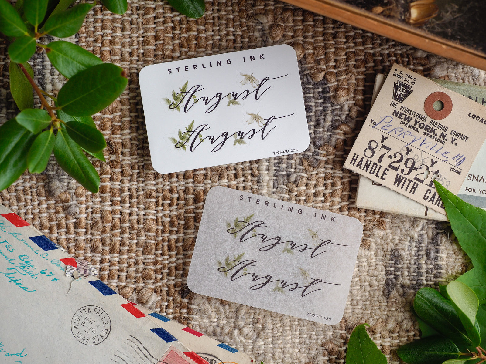 August month stickers featuring elegant script lettering, bordered by natural green watercolor foliage on various creamy white and rustic kraft paper backgrounds.