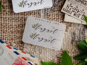 Rustic August month planner sticker featuring brown script calligraphy and delicate green botanical leaf illustrations for journaling.