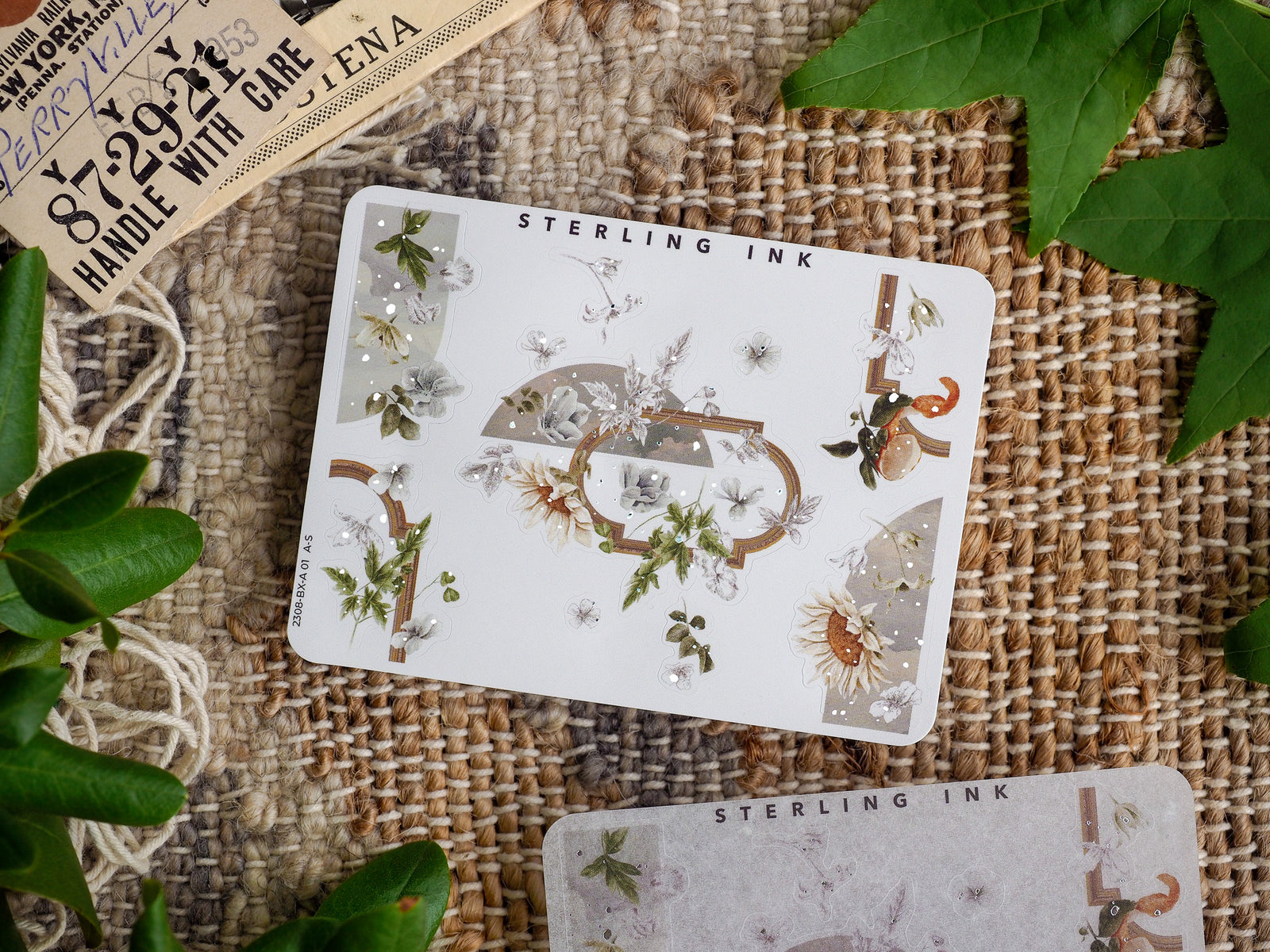 Elegant corner sticker sheet (August 2023) featuring intricate silver foil accents and a seasonal botanical arrangement of white flowers, delicate leaves, and rustic natural elements.