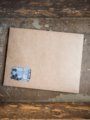 Light brown kraft cardstock featuring a small, rectangular sticker with distressed, layered print designs suitable for scrapbooking or journaling.