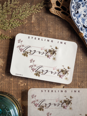 Delicate August month sticker sheet featuring natural watercolor wildflowers, leafy greenery, and the cursive month name for journal decorating.