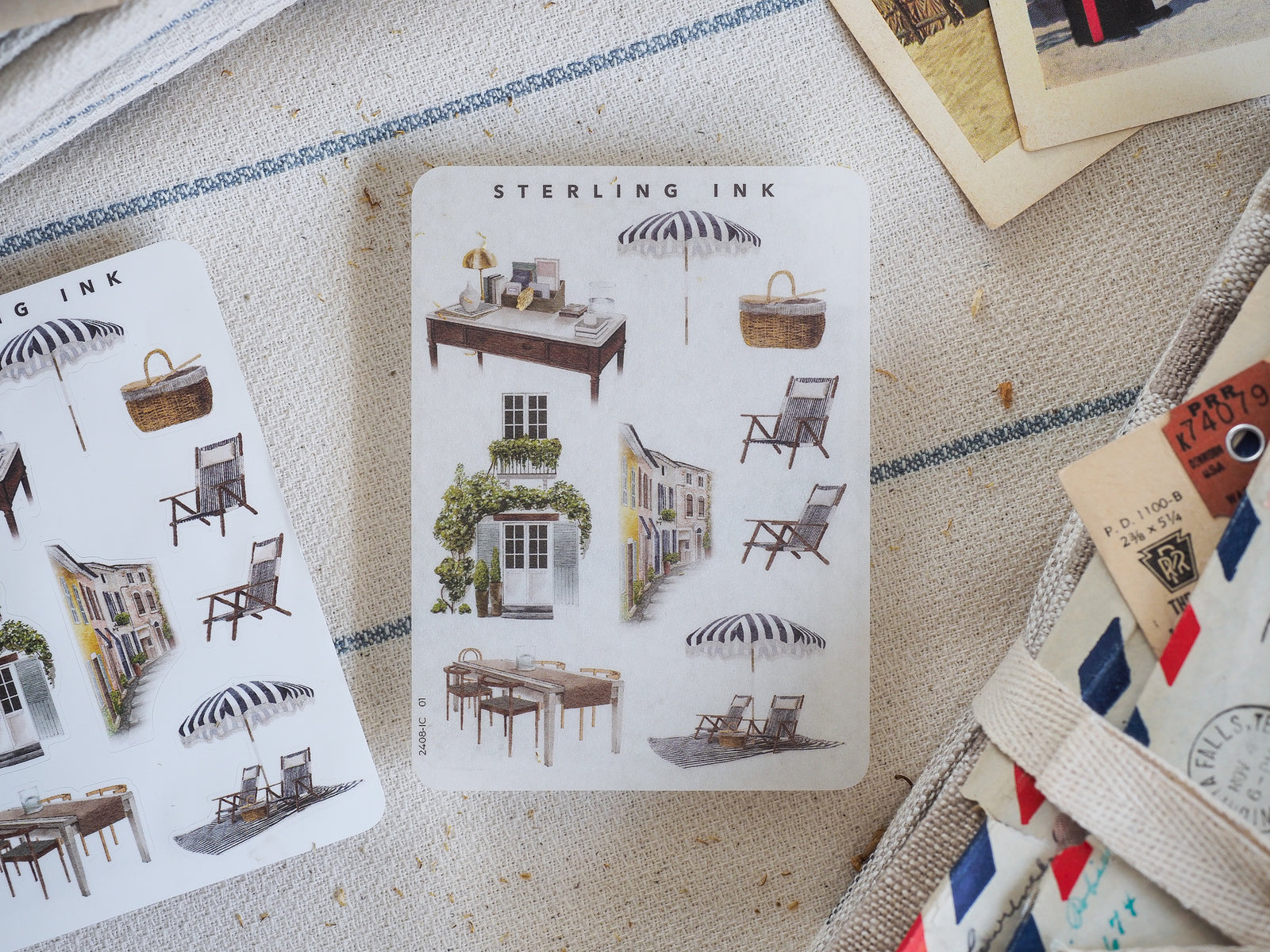 A detailed sticker set of black and white illustrated summer elements, featuring picnic tables, lounge chairs, quaint seaside buildings, and striped sunshades.