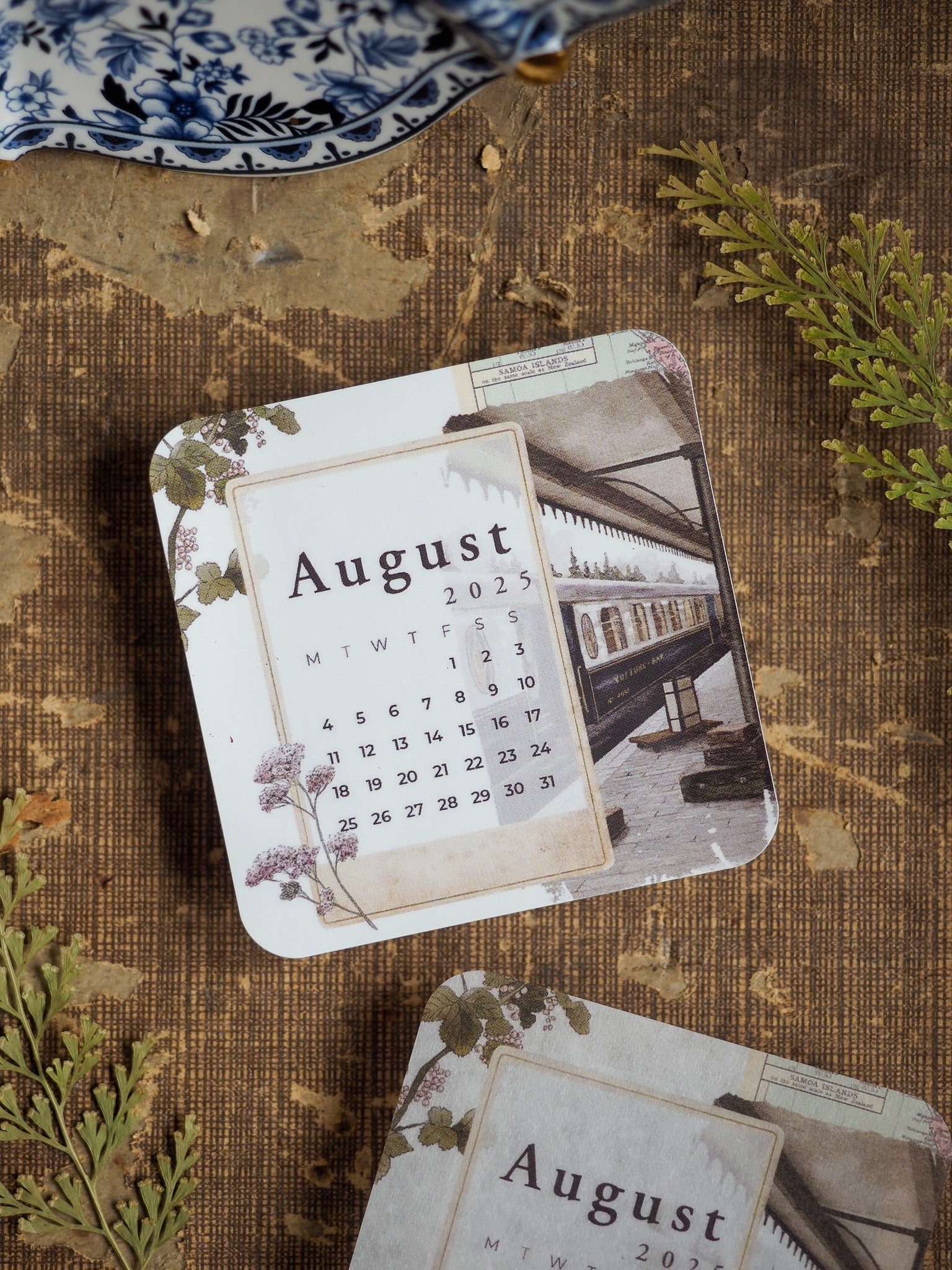 Vintage August 2025 calendar sticker featuring a clean month grid and an antique illustration of a railway station and steam train.