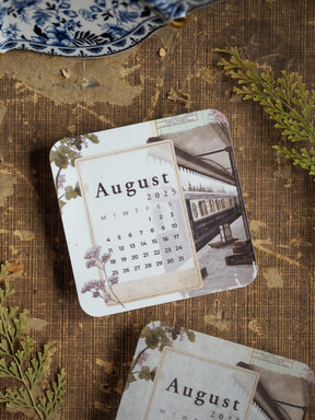Vintage August 2025 calendar sticker featuring a clean month grid and an antique illustration of a railway station and steam train.