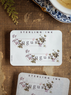 Aesthetic August planner sticker set featuring "Sterling Ink" text and delicate watercolor floral designs of purple and green leaves.