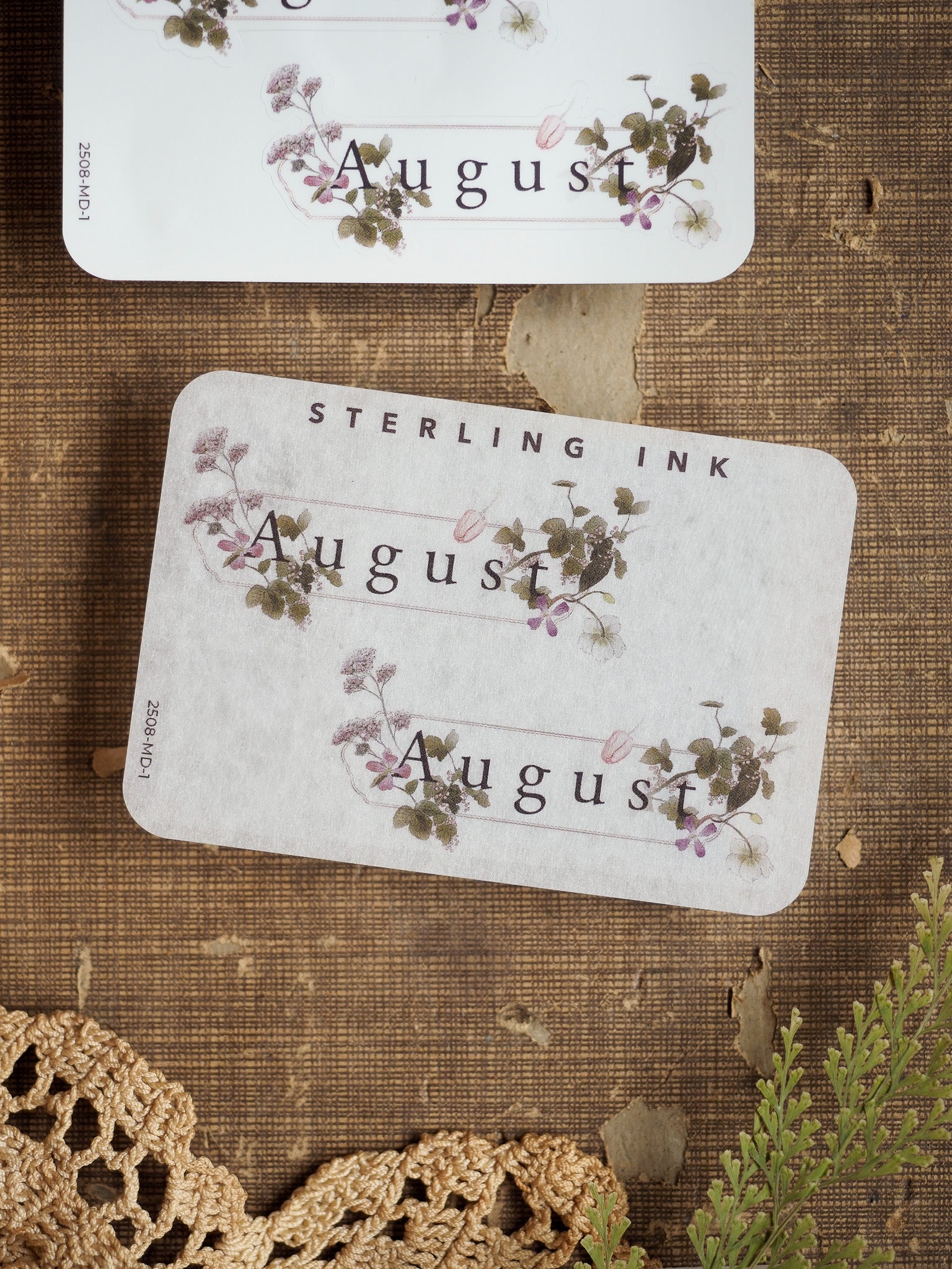 Delicate August month stickers with an elegant floral wreath design, featuring printed lavender and green wildflower illustrations on a pale cream background.