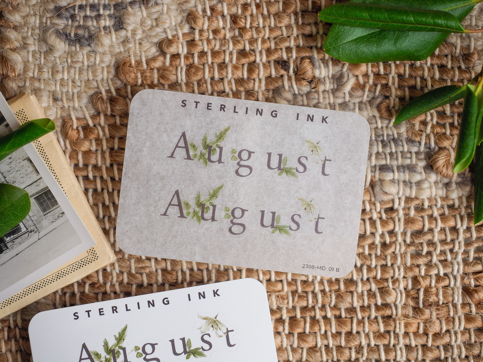 August month sticker featuring elegant, nature-themed green leaf illustrations on pale, neutral kraft paper.