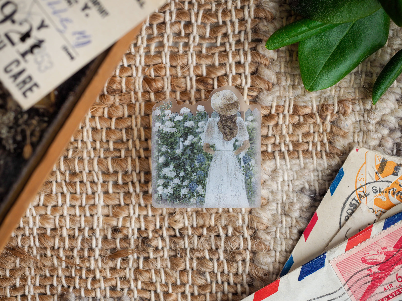 Die-cut vinyl sticker featuring a vintage depiction of a woman in a light dress surrounded by abundant white flowers in a spring meadow scene.