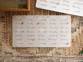 Decorative set of light beige stickers detailing the days of the week (Monday through Sunday) with a vintage, hand-lettered floral design perfect for August planning.