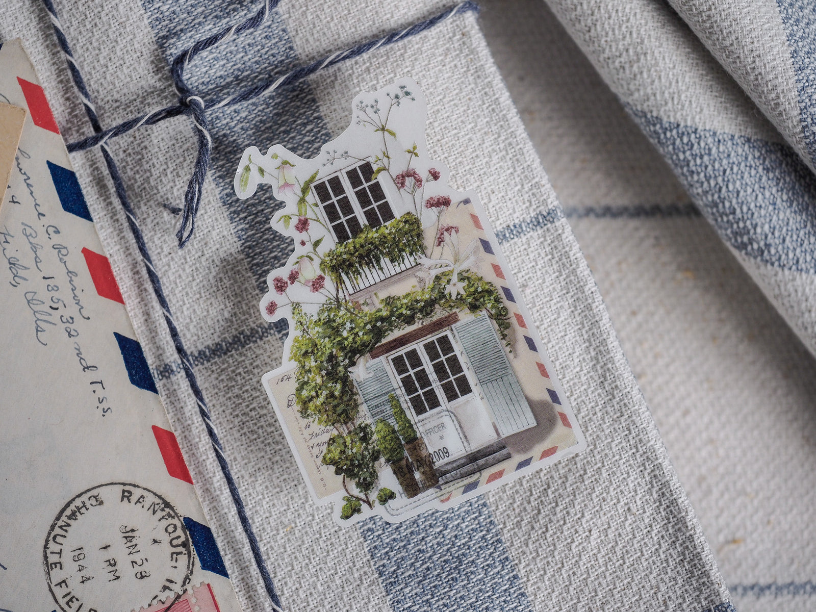 Die-cut vinyl sticker showing a charming, detailed cottage illustration with green climbing vines, flowers, and a rustic, vintage feel.