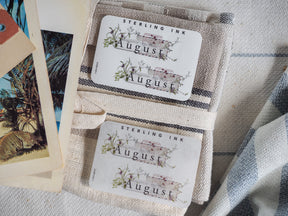 Cream-colored August month sticker set by Sterling Ink, decorated with delicate green watercolor flora surrounding the title for elegant journaling and planning.