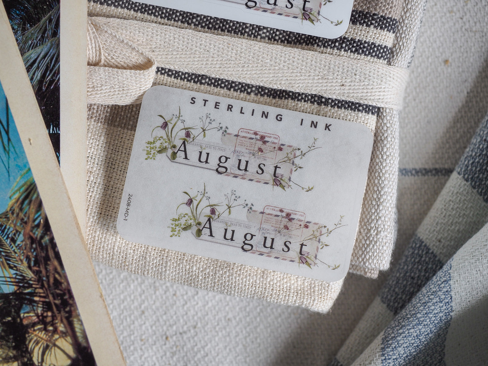 Elegant August sticker featuring delicate green foliage and small flowers framing the month name, ideal for planners and journal decorating.