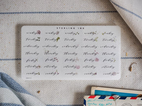 Whimsical sheet of hand-lettered labels in muted sepia ink, showcasing all seven days of the week for August 2024.