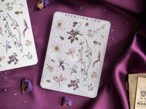 Elegant botanical sticker set featuring detailed engraved line art of leaves, stems, and flowers printed on a pale, antique cream background.