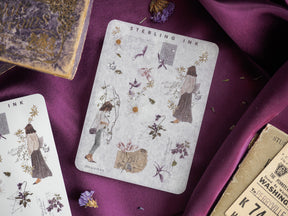 Vintage sticker sheet featuring botanical illustrations, delicate figures, and accents of sparkling silver foil on a muted gray background.