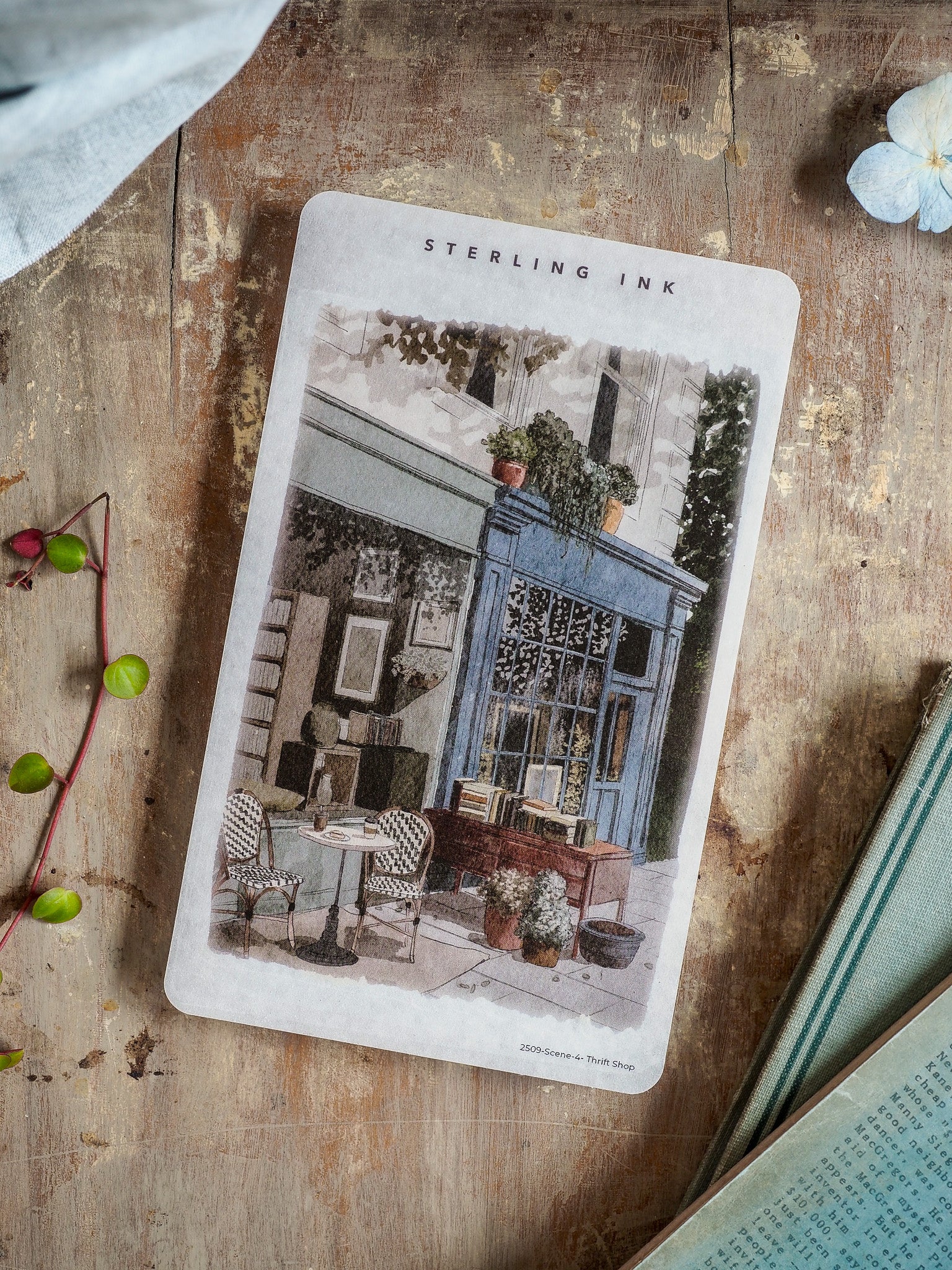 Vintage black and white illustration depicting a charming thrift shop facade, complete with window displays and quaint outdoor cafe seating.