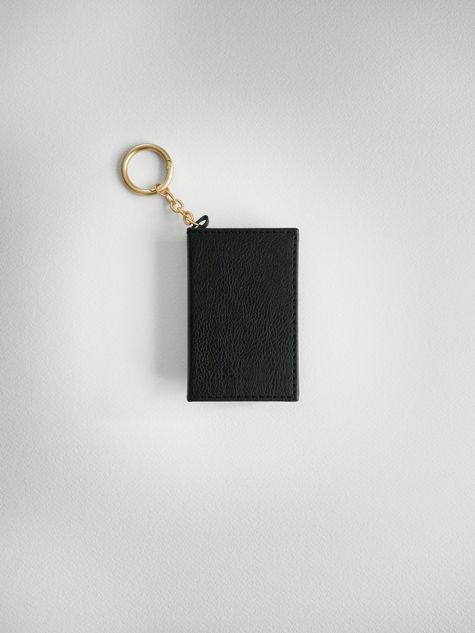 A black textured leather keychain pouch with a gold-tone split key ring and chain, shown against a light gray textured background.
#Color_Onyx