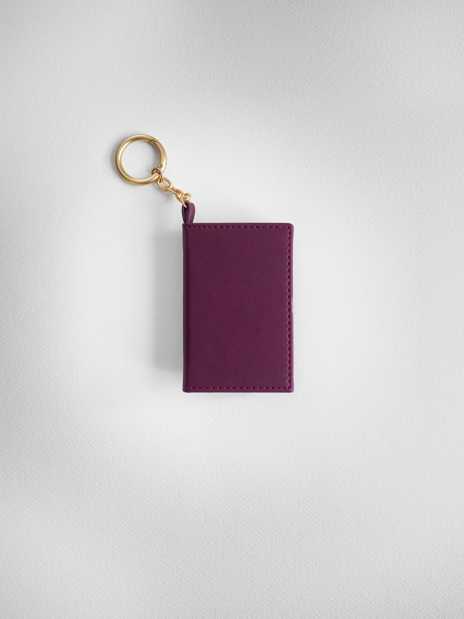 A small rectangular purple leather card holder or wallet keychain with a gold-tone split ring and chain, shown on a light gray textured background.
#Color_Mulberry