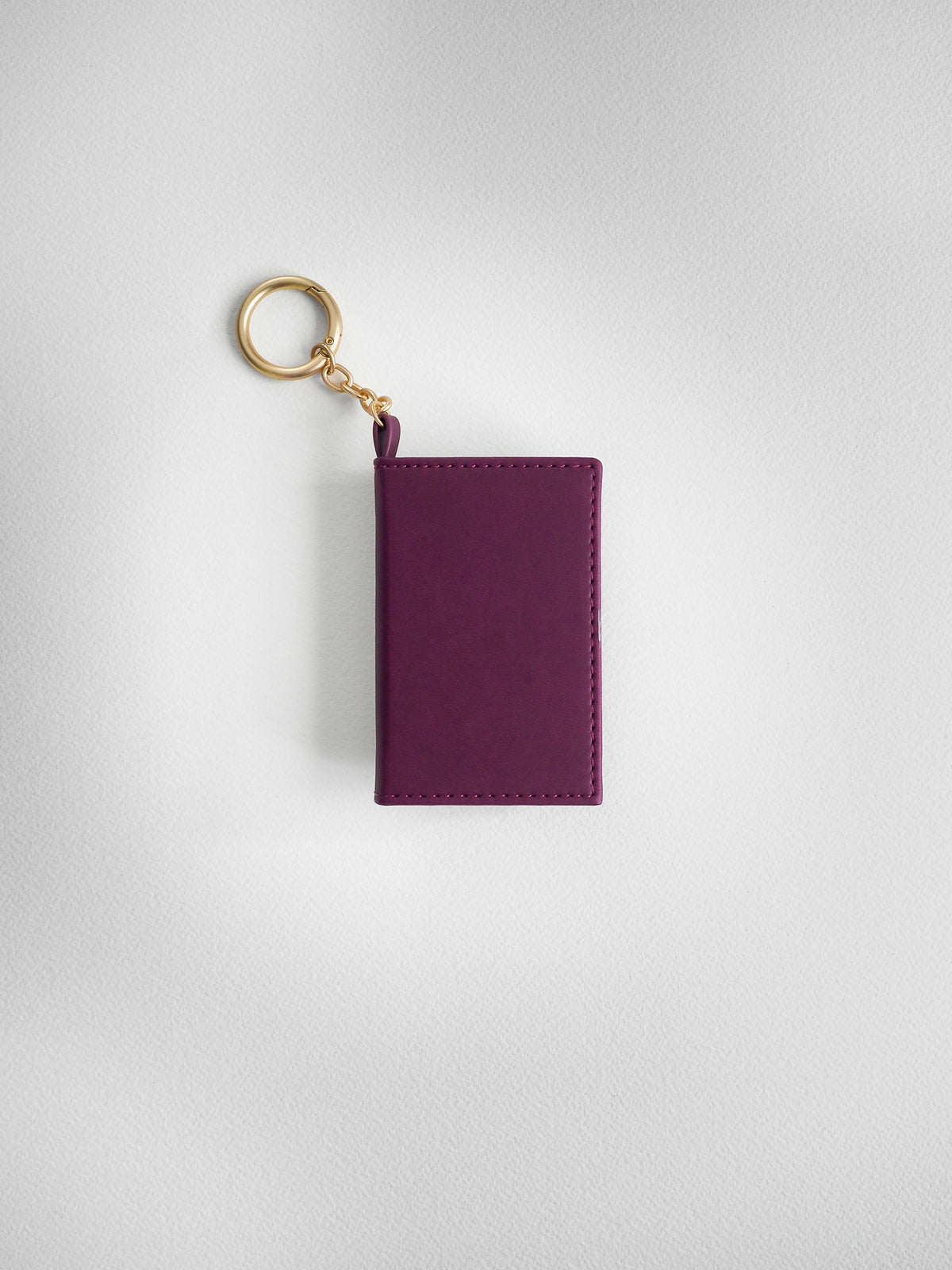 A small rectangular purple leather card holder or wallet keychain with a gold-tone split ring and chain, shown on a light gray textured background.
#Color_Mulberry