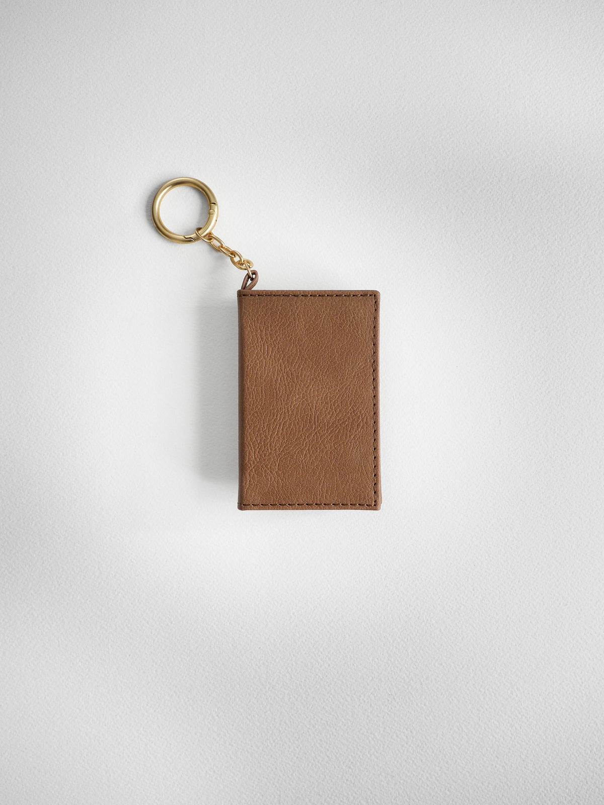 A brown leather card holder keychain with a gold-tone split ring and chain, shown on a light gray textured background.
#Color_Caramel
