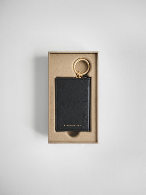 A black textured leather keychain with a gold-tone key ring, presented inside a beige cardboard gift box on a light gray background.
#Color_Onyx
