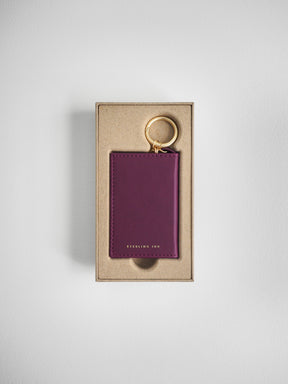 A purple leather card holder keychain with a gold key ring, presented in a kraft paper box on a light gray background.
#Color_Mulberry