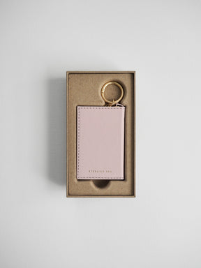 A light pink leather card holder keychain with a gold split ring, presented inside a brown kraft paper gift box on a light gray background.
#Color_Fairyfloss