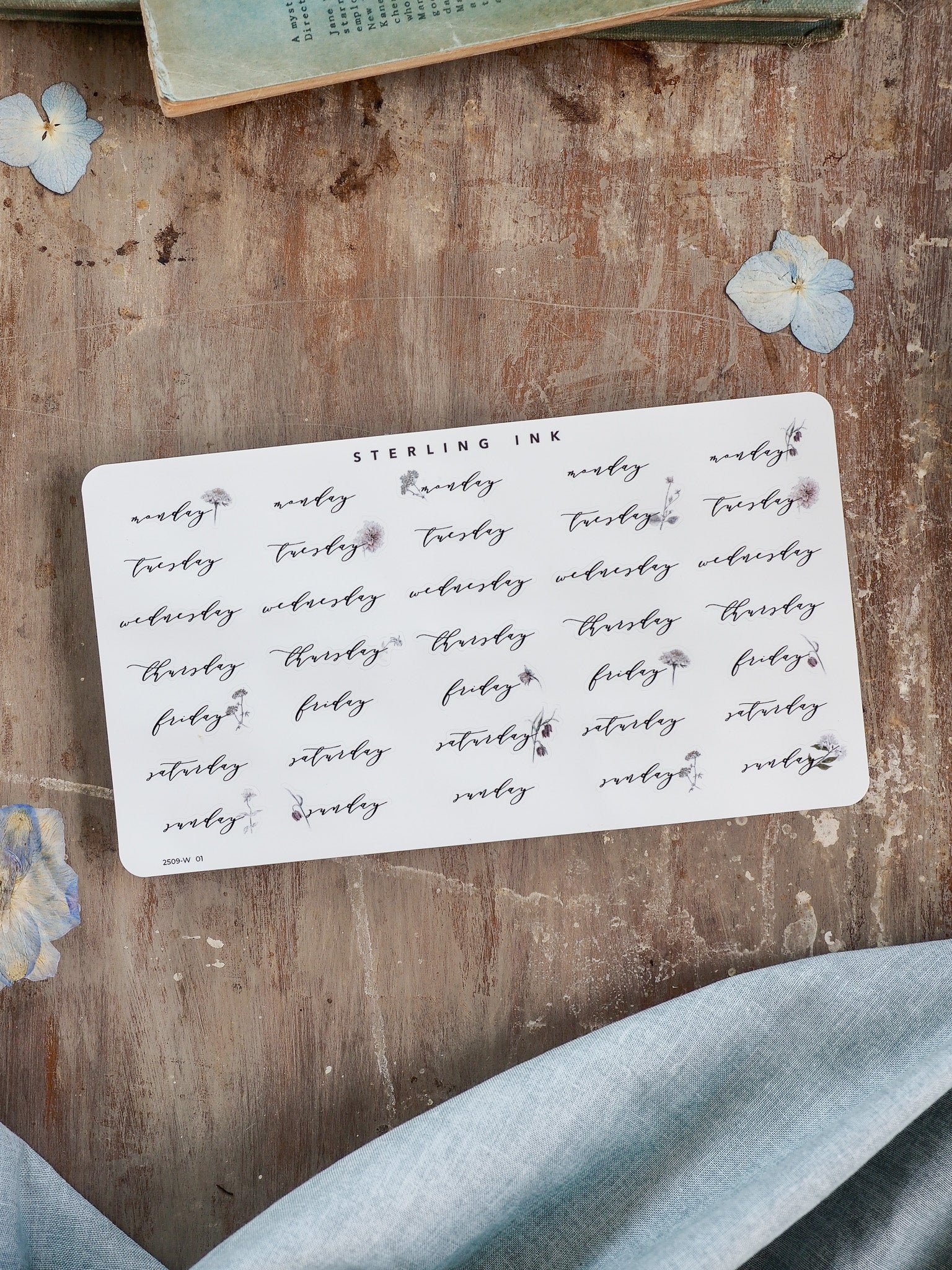 Decorative sheet of white planner stickers featuring black cursive typography for weekdays and delicate accompanying floral sprigs, ideal for journaling and organization.