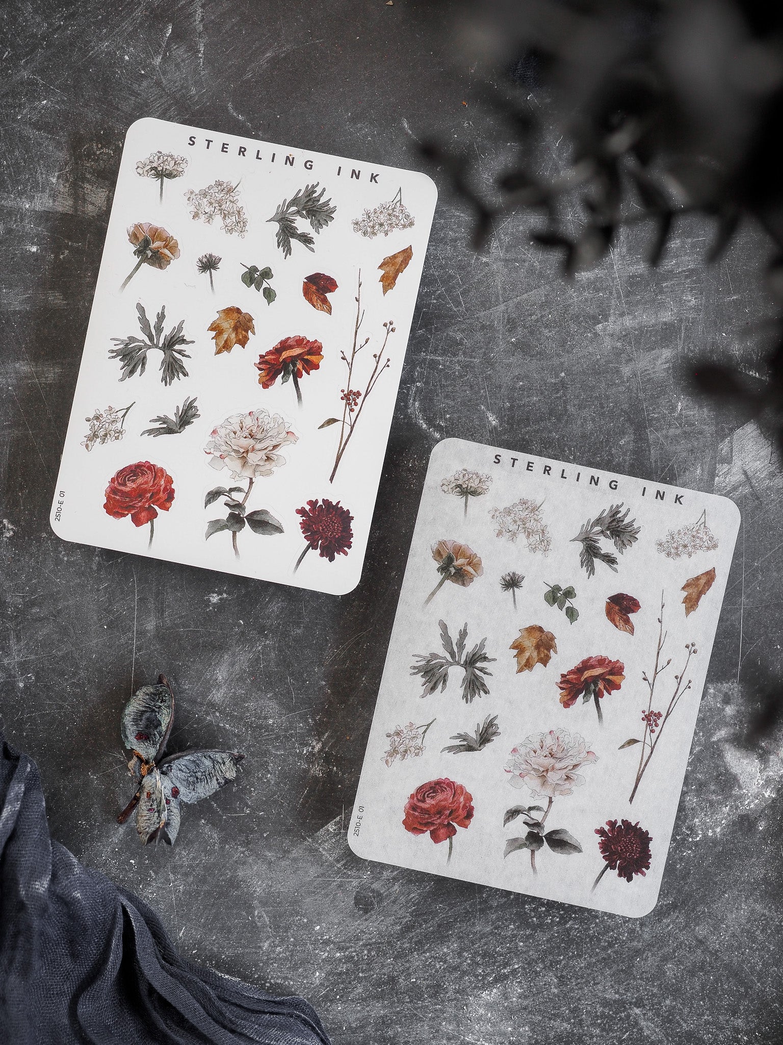 Two white sticker sheets featuring an autumn-themed collection of detailed botanical elements, including rich red and rust-colored flowers and varied fall foliage.
