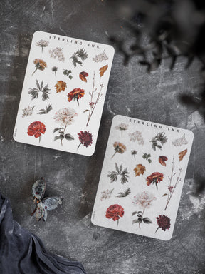 Two white sticker sheets featuring an autumn-themed collection of detailed botanical elements, including rich red and rust-colored flowers and varied fall foliage.