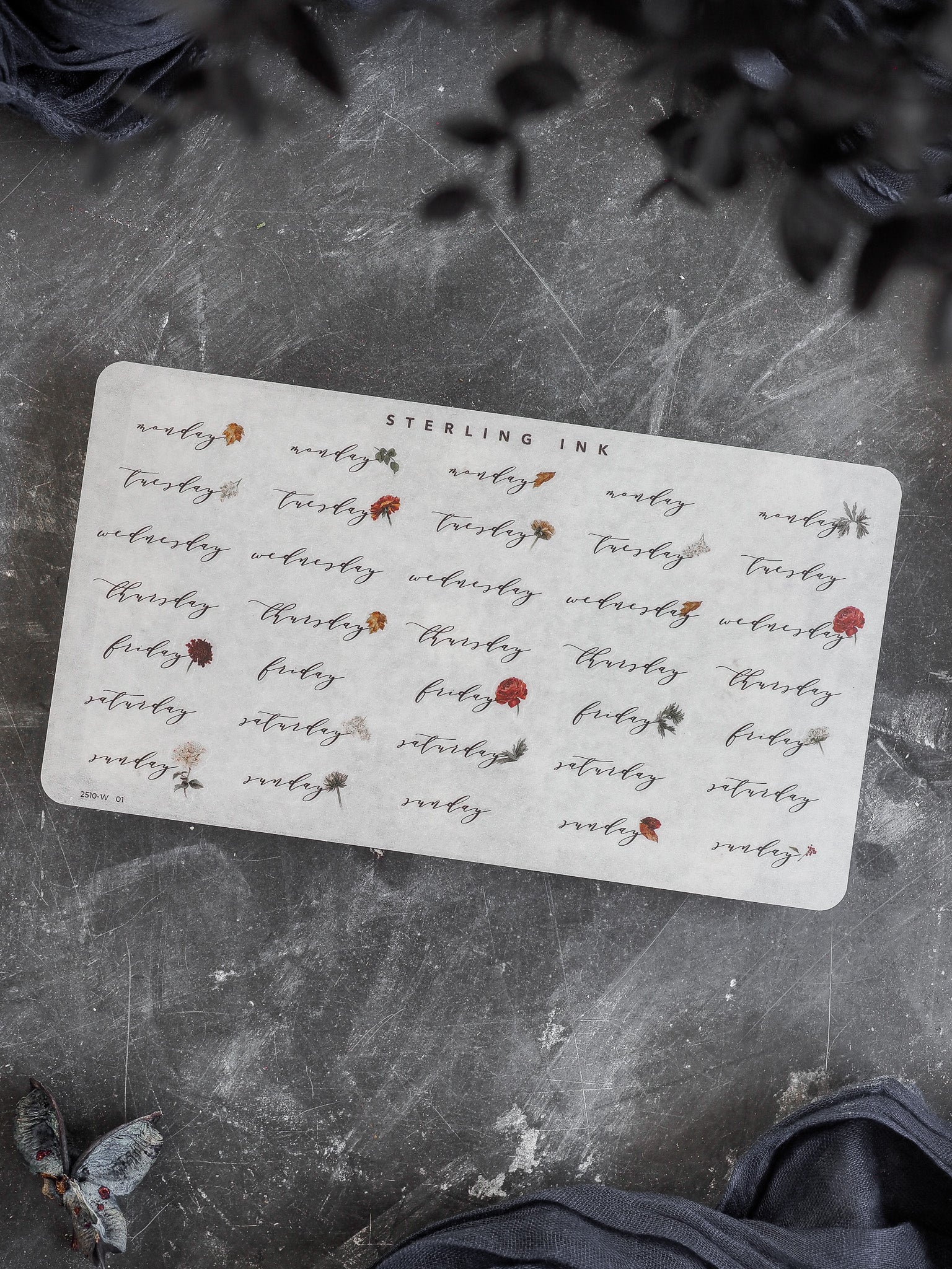 Elegant calendar stickers printed on white cardstock, detailing days of the week and dates in a rustic, handwritten script with delicate leaf motifs for planning.