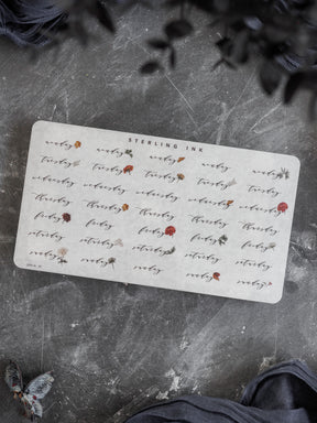 Elegant calendar stickers printed on white cardstock, detailing days of the week and dates in a rustic, handwritten script with delicate leaf motifs for planning.