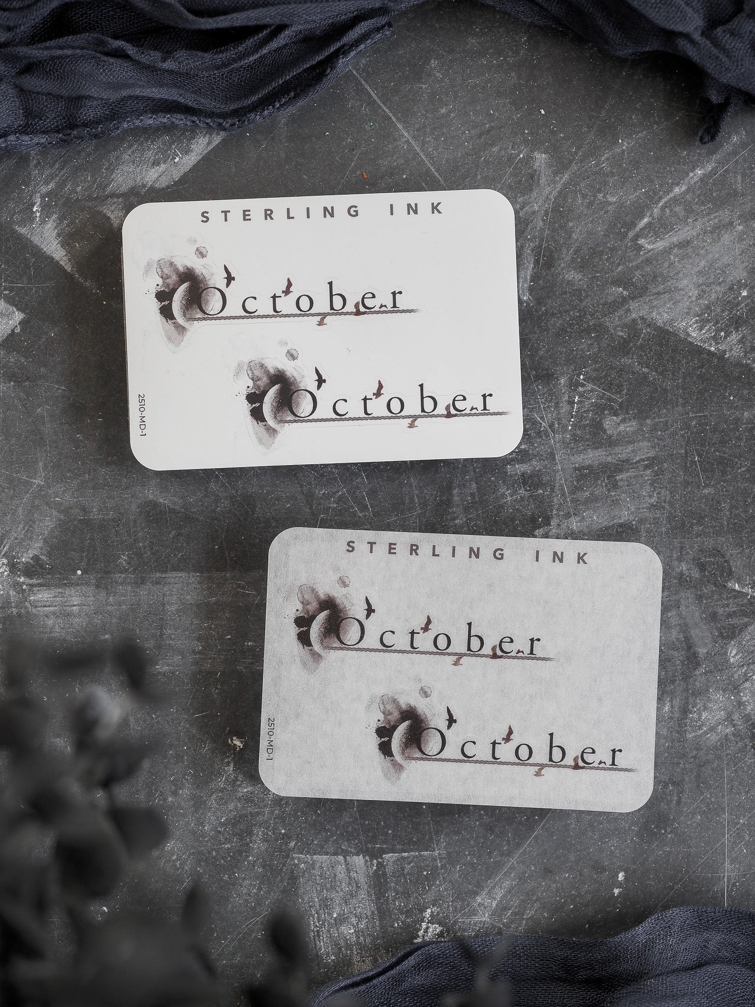 Cream-colored "October" month sticker featuring a rustic, distressed vintage design with dark ink lettering and small decorative bat silhouettes perfect for a fall theme.