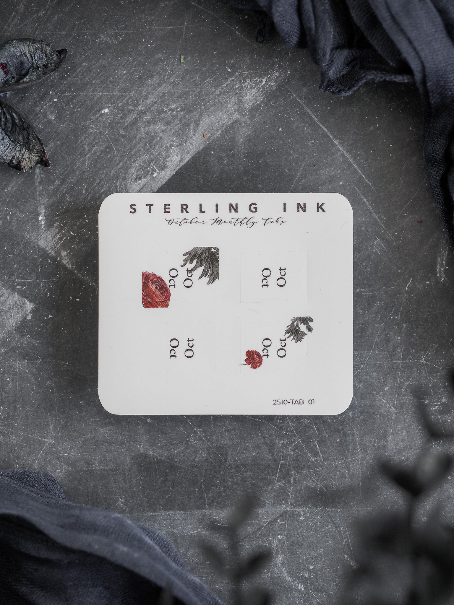 A white sticker sheet featuring "STERLING INK" October tabs with an autumnal theme, decorated with small, detailed clusters of deep red and brown falling leaves.