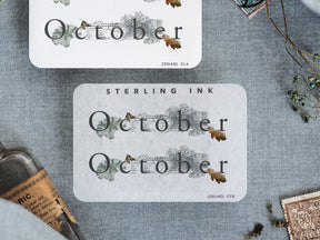 Rustic watercolor sticker for October, featuring the word "October" surrounded by delicate autumn foliage and earth-toned greenery.