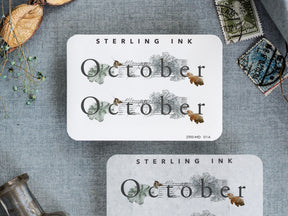 Rustic October month sticker with elegant script and delicate surrounding watercolor illustrations of autumn foliage in muted greens and browns.