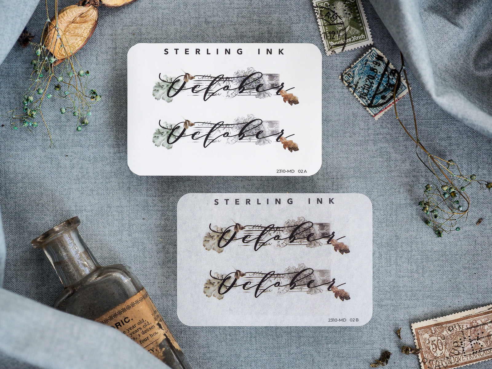 Elegant "October" month stickers with flowing script typography accented by rustic, muted watercolor washes and autumnal floral sprigs.