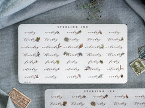 A decorative sheet of weekly sticker labels for planners, featuring the days of the week (Monday-Sunday) in a rustic, hand-lettered style with delicate brown and green botanical accents.