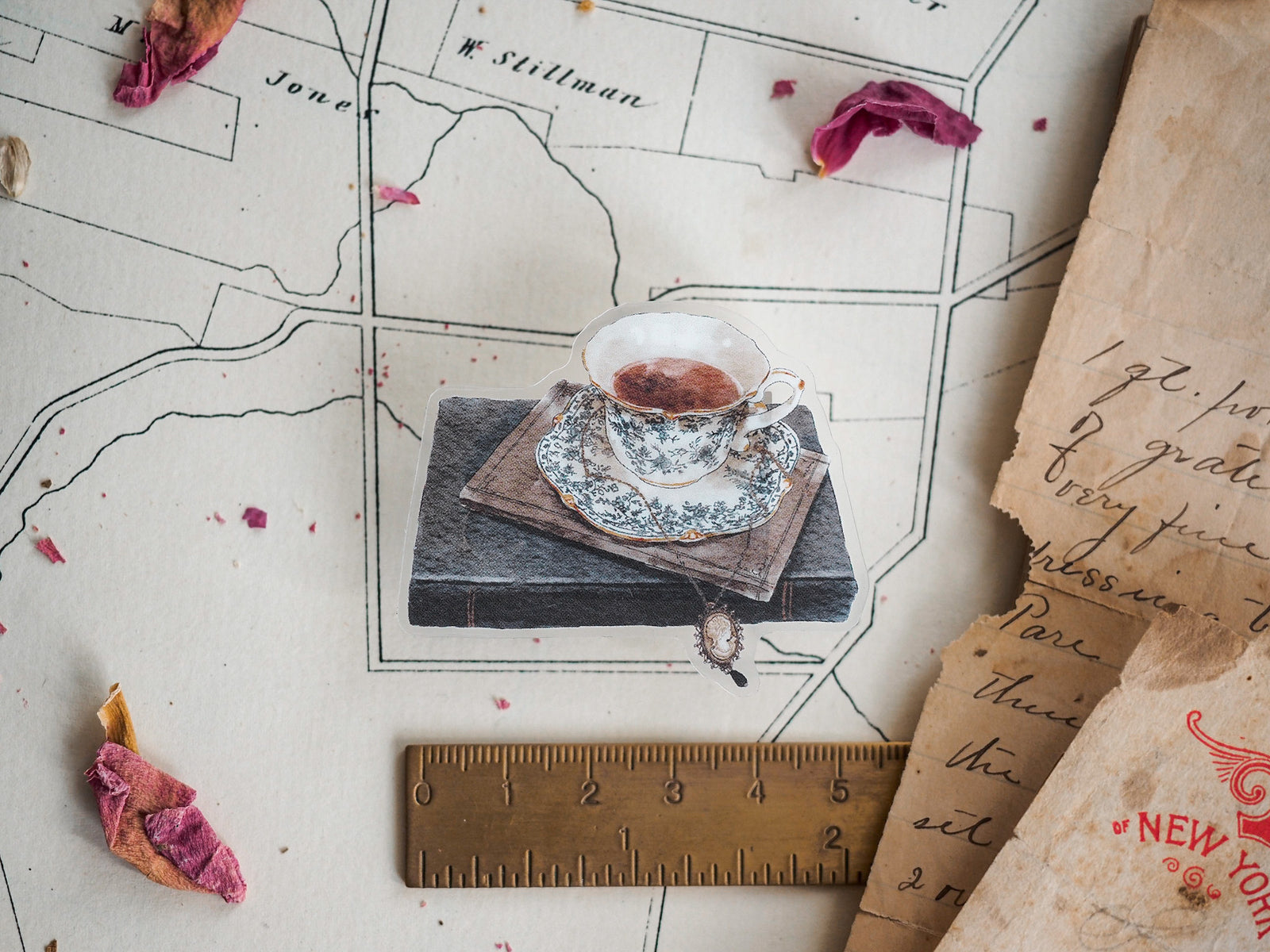 Detailed die-cut sticker featuring a vintage china teacup and saucer with a warm beverage, displayed atop a stack of aged books.