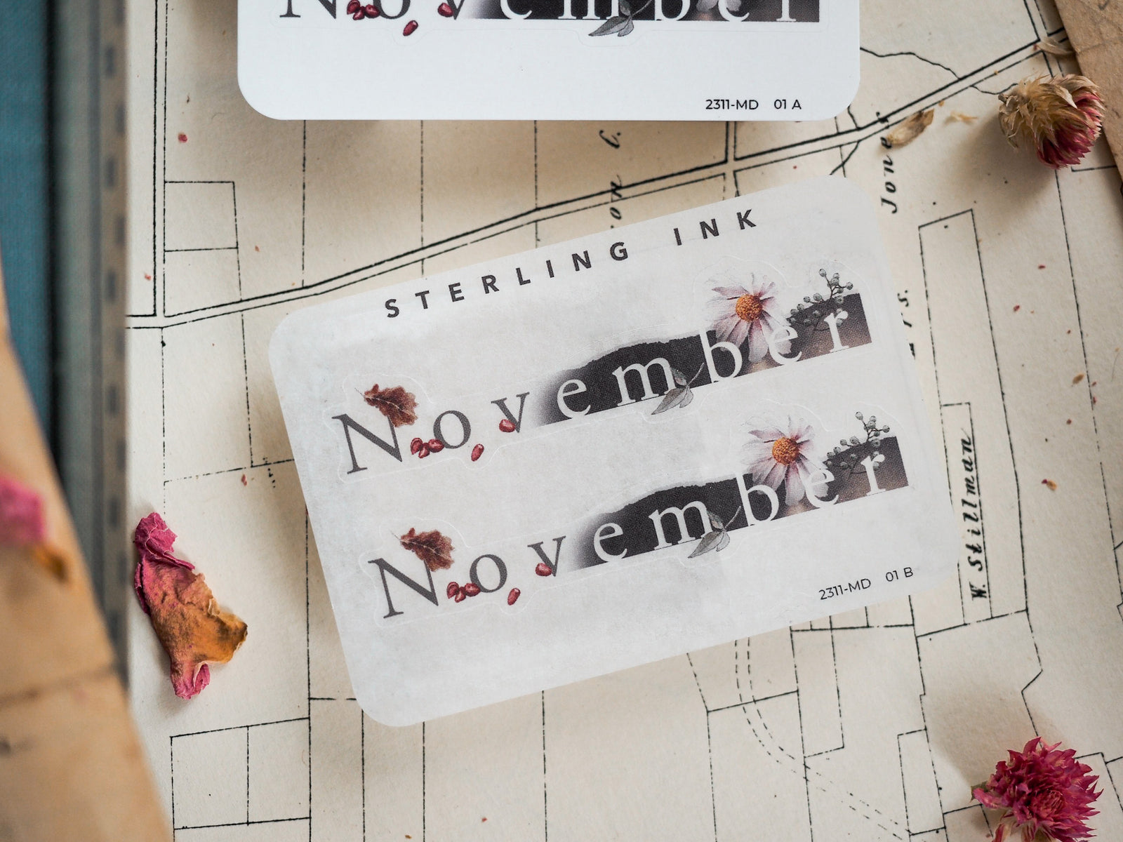 Seasonal "November" month sticker featuring rustic typography and delicate accents of dried leaves and pale pink floral illustrations for autumn journaling.